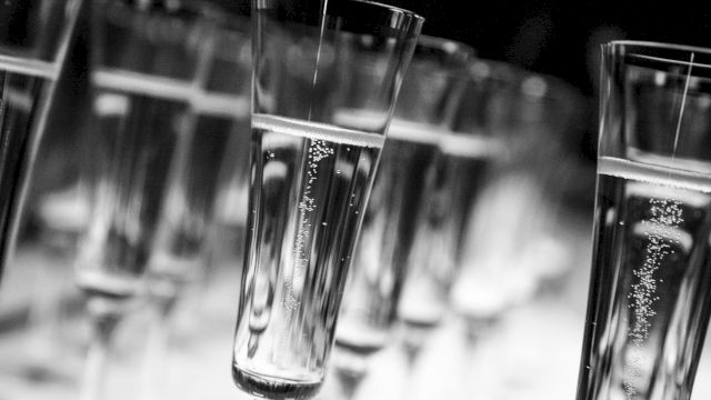 A row of elegant champagne flutes stands upright in a blurred setting, showcasing their tall stems and bubbly contents, evoking a celebratory toast.