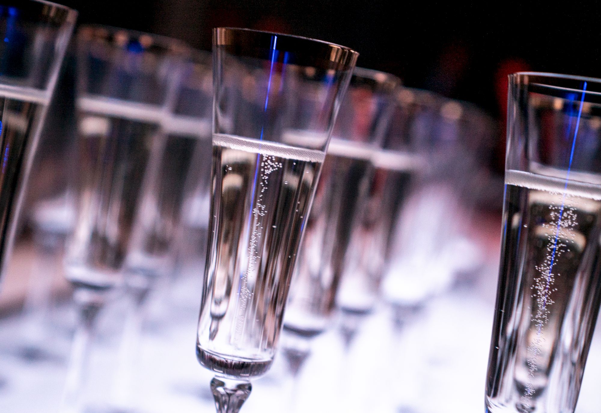 A row of champagne flutes with bubbles rising, set in a festive, blurred backdrop.