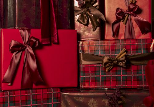 A pile of wrapped presents in red, burgundy, and plaid with satin bows, layered and festive for a holiday gift display.