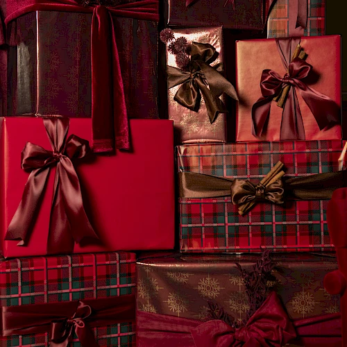A pile of wrapped presents in red, burgundy, and plaid with satin bows, layered and festive for a holiday gift display.