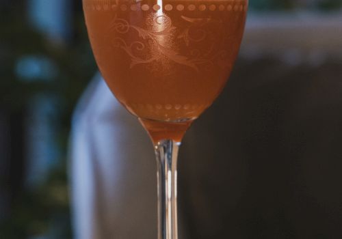 A cocktail in a stemmed glass with a lime wedge garnish, set on a wooden table.