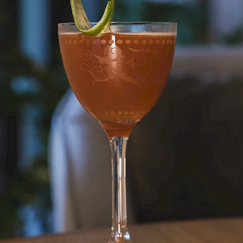 A cocktail in a stemmed glass with a lime wedge garnish, set on a wooden table.