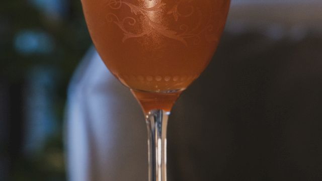 A cocktail in a stemmed glass with a lime wedge garnish, set on a wooden table.