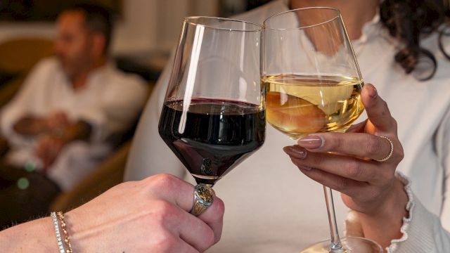 Two people clink wine glasses in a warm, cozy setting; smiles, soft lighting, and relaxed vibes as they toast together.