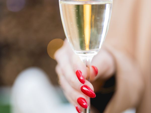 A hand with red nails holds a champagne flute, toasting the glass with bubbly rising inside.