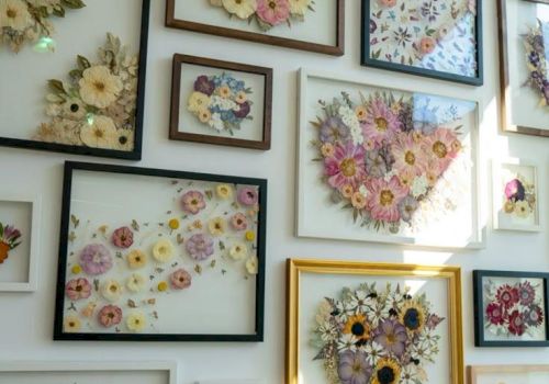 A wall filled with framed floral arrangements, many bouquets in pastel tones, arranged in varied frame sizes and styles.