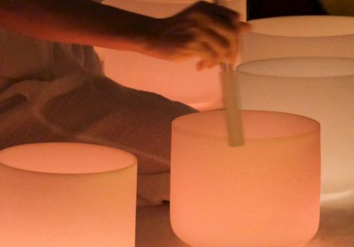 People are relaxing in a dim, candlelit setting, someone stirs a large frosted glass with a wooden tool near glowing candles.