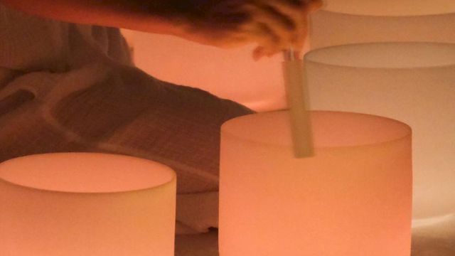 People are relaxing in a dim, candlelit setting, someone stirs a large frosted glass with a wooden tool near glowing candles.