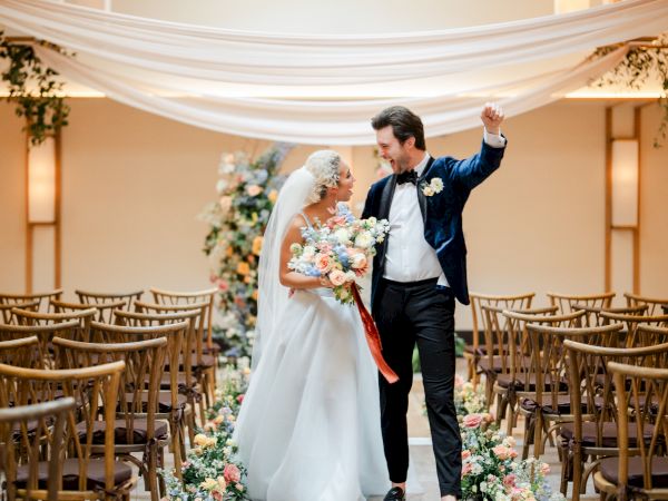 A bride and groom sharing a kiss at the altar after a wedding, floral arches, aisle flowers, and guests seated on both sides.