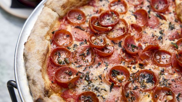 A pepperoni-tomato pizza with a golden crust, served on a metal tray with a side of dip and toppings nearby.