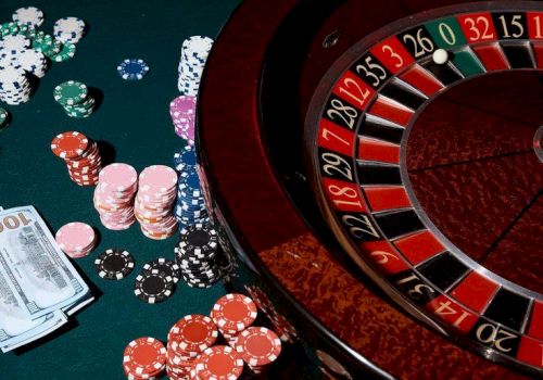 Roulette table with chips, cards, and money scattered, casino glow, hands placing bets around the wheel, classic gambling scene tonight.