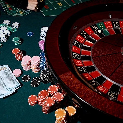 Roulette table with chips, cards, and money scattered, casino glow, hands placing bets around the wheel, classic gambling scene tonight.