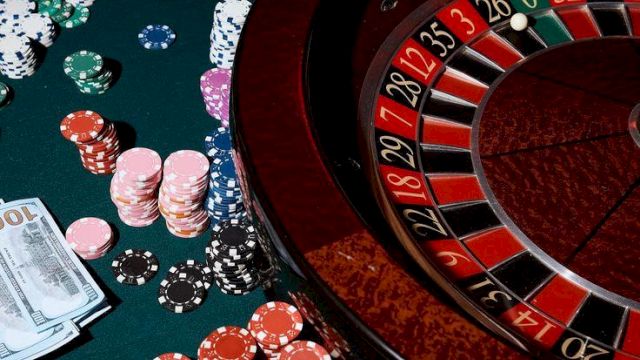 Roulette table with chips, cards, and money scattered, casino glow, hands placing bets around the wheel, classic gambling scene tonight.