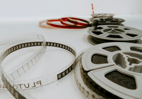 A collection of vintage film reels and a transparency strip laid out on a white surface, with one red-tinted reel in the background, ending this sentence.