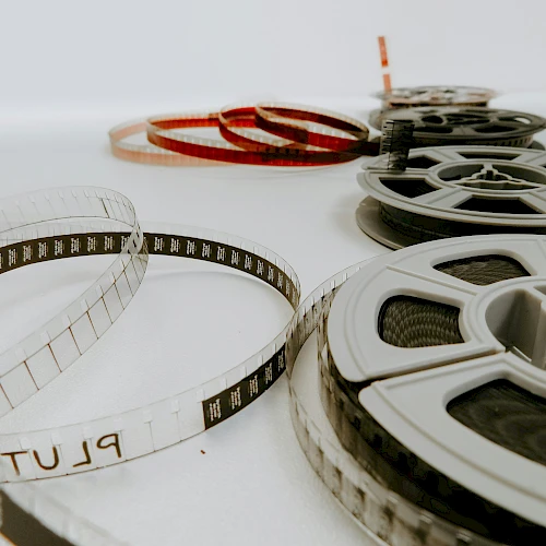A collection of vintage film reels and a transparency strip laid out on a white surface, with one red-tinted reel in the background, ending this sentence.