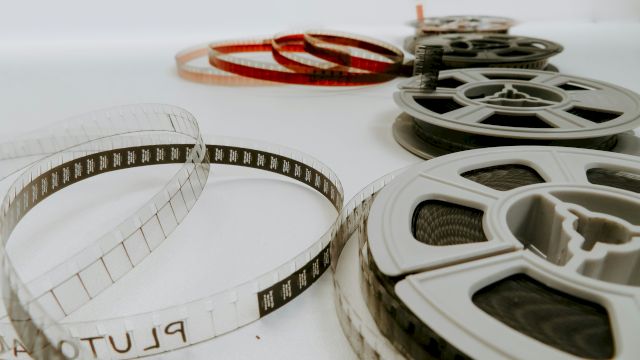 A collection of vintage film reels and a transparency strip laid out on a white surface, with one red-tinted reel in the background, ending this sentence.