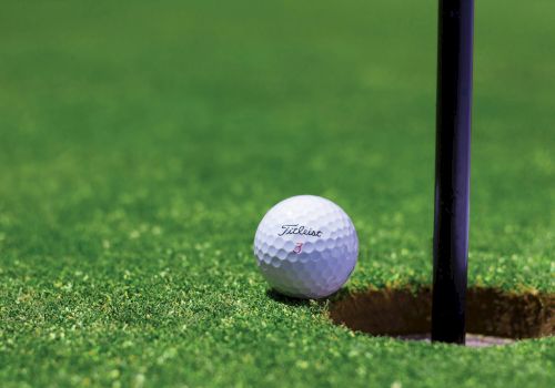 A golf ball rests near a hole on a manicured green, with a flagstick nearby.