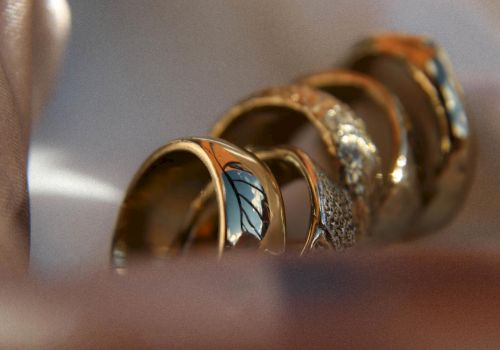 A close-up of several stacked rings with colorful gemstones and intricate designs, resting in soft light on a smooth surface.