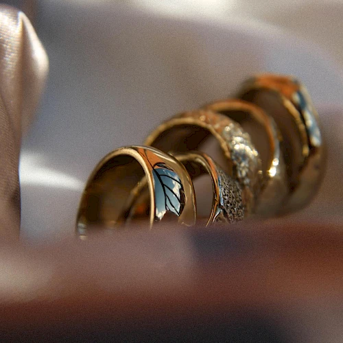 A close-up of several stacked rings with colorful gemstones and intricate designs, resting in soft light on a smooth surface.