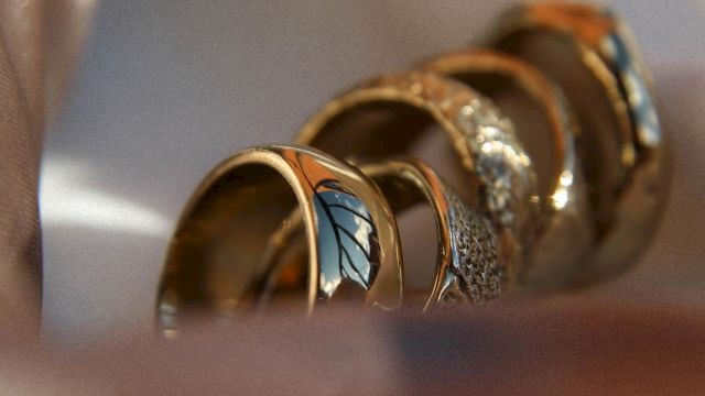 A close-up of several stacked rings with colorful gemstones and intricate designs, resting in soft light on a smooth surface.