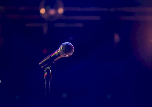 A close-up of a microphone on a stand against a dark blue stage backdrop, ready for a performance.