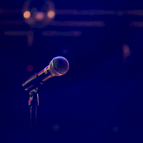 A close-up of a microphone on a stand against a dark blue stage backdrop, ready for a performance.