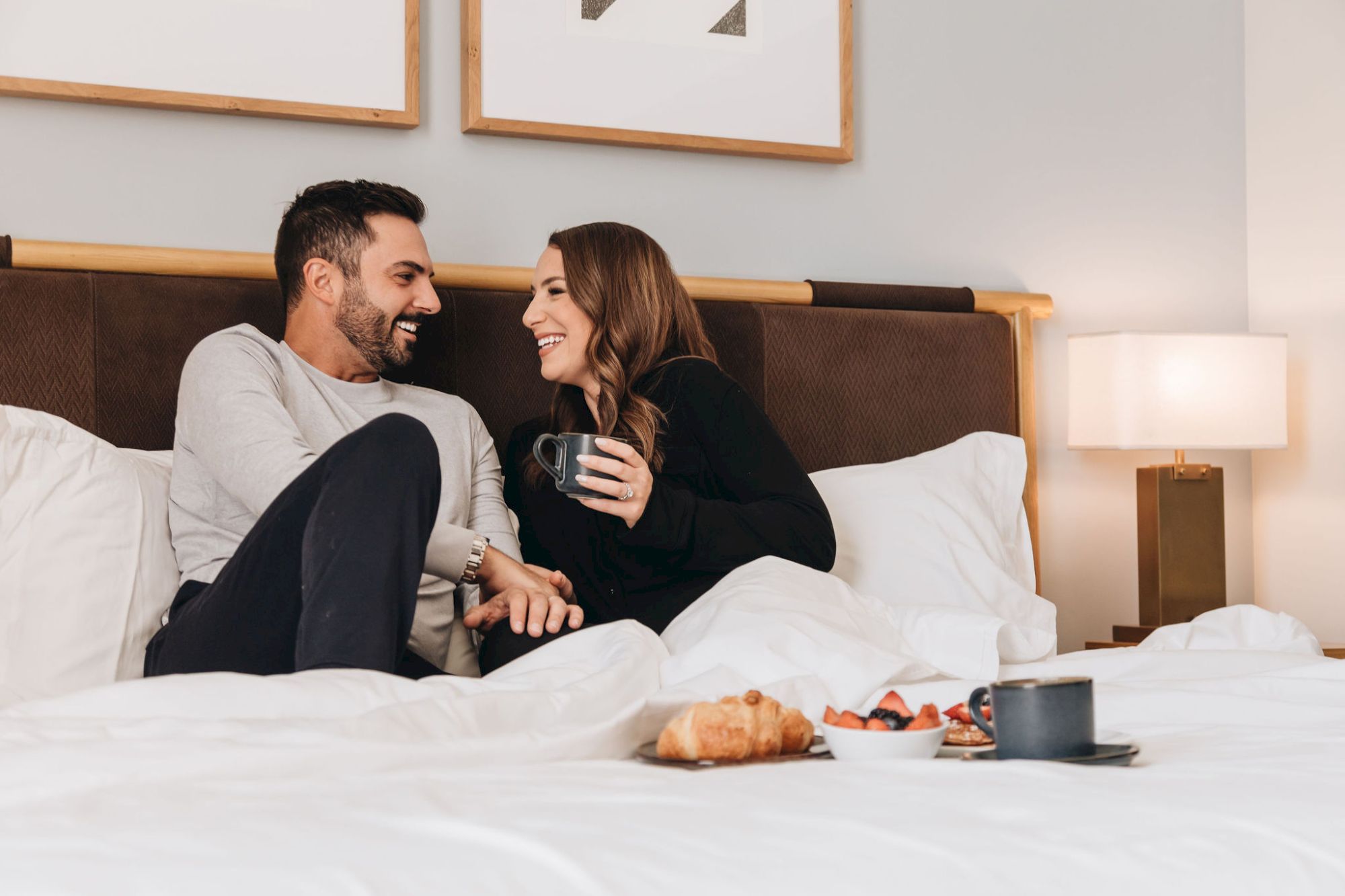 A couple relaxing in bed, sharing a coffee and breakfast pastries together.