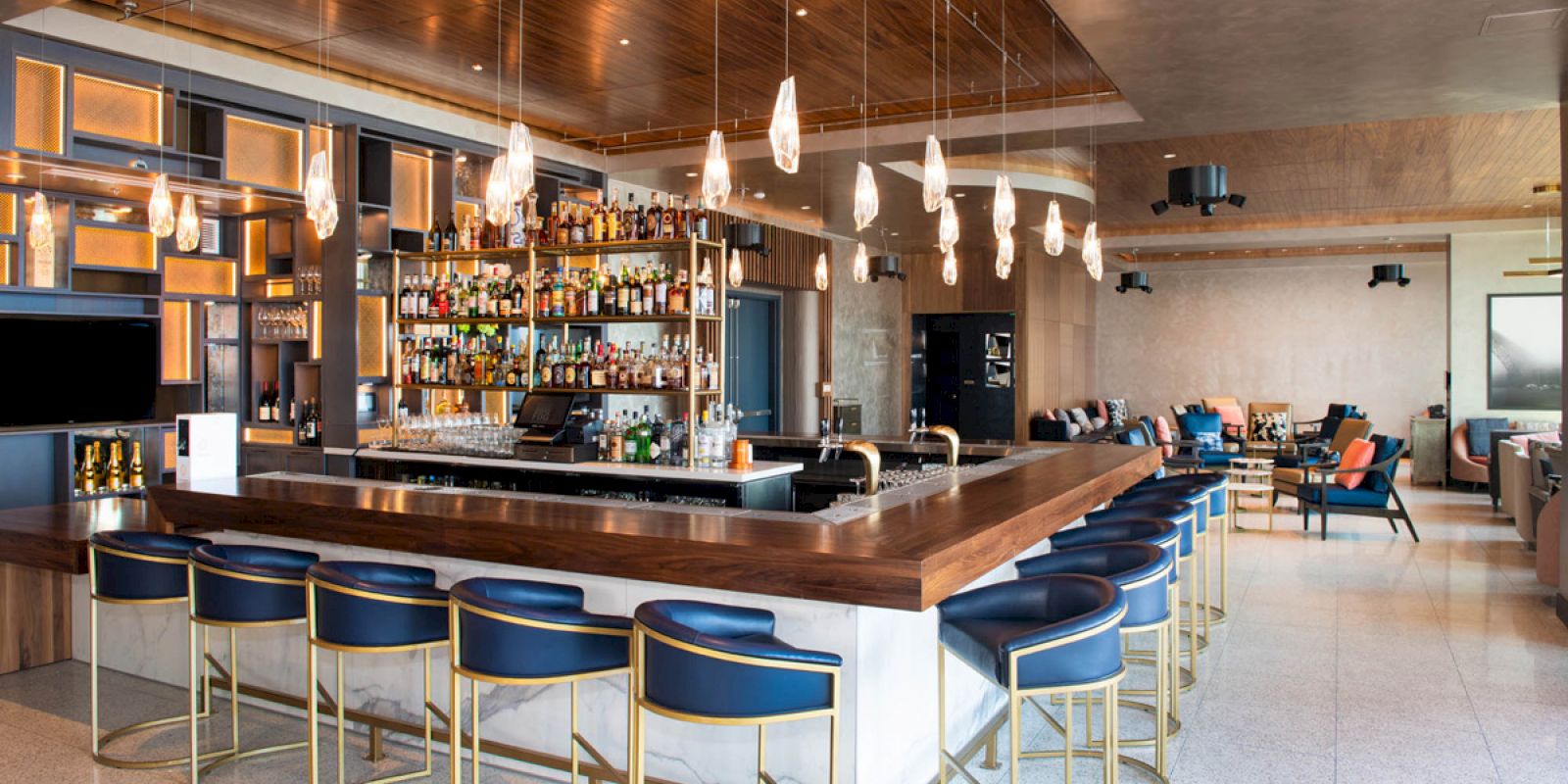 A modern bar with blue stools, pendant lights, and a well-stocked liquor shelf, set in a stylish lounge area.