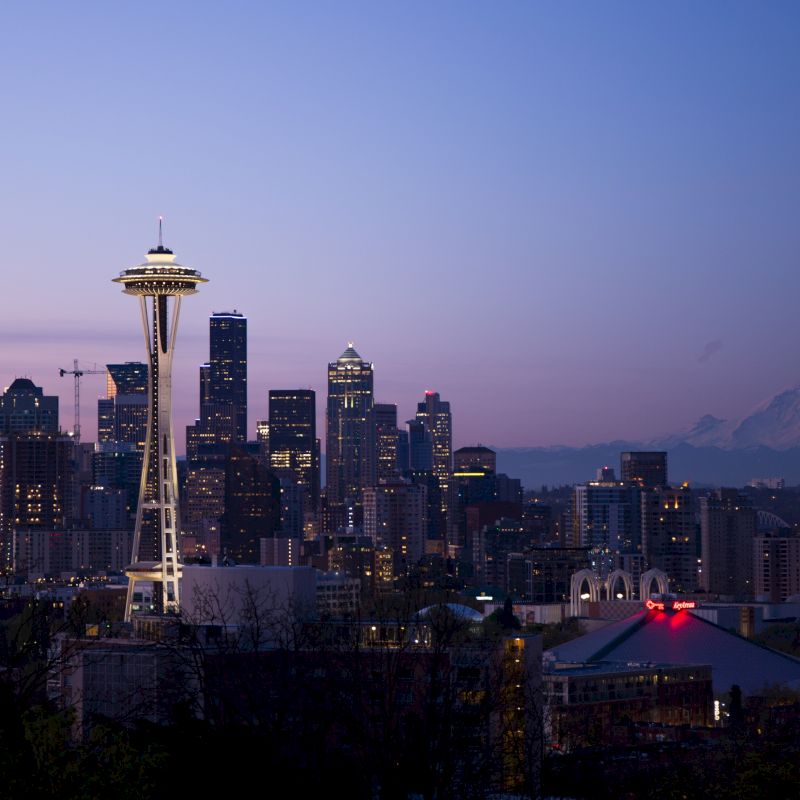 Seattle skyline at dusk with the Space Needle prominently visible, and Mount Rainier in the background under a twilight sky.