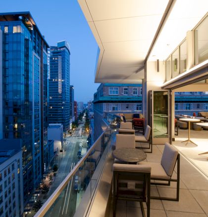 A modern outdoor terrace with seating overlooks a cityscape with tall buildings at dusk.