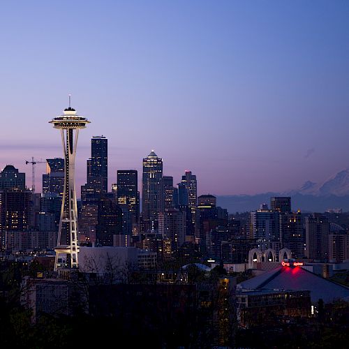 The image shows the Seattle skyline at dusk with the Space Needle prominently visible and Mount Rainier in the background.