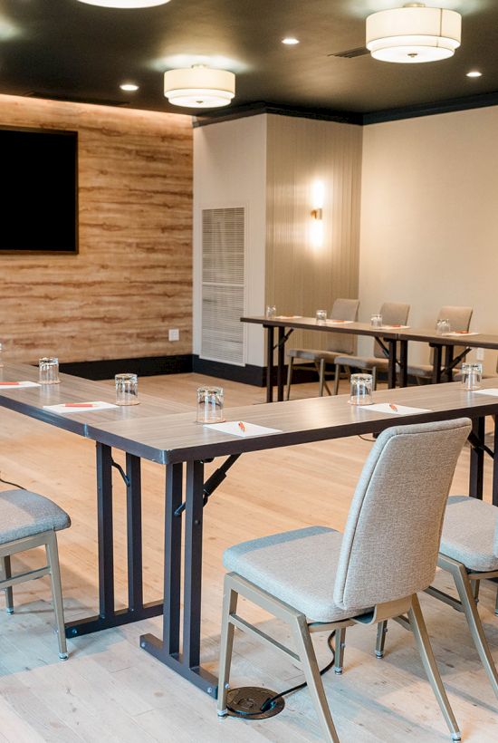 A modern conference room with a U-shaped table setup, light gray chairs, glassware, a wall-mounted screen, and warm wood accents.